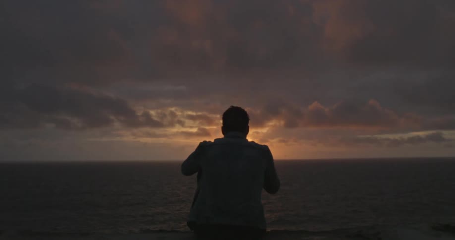Man sitting down watching the sunset over water