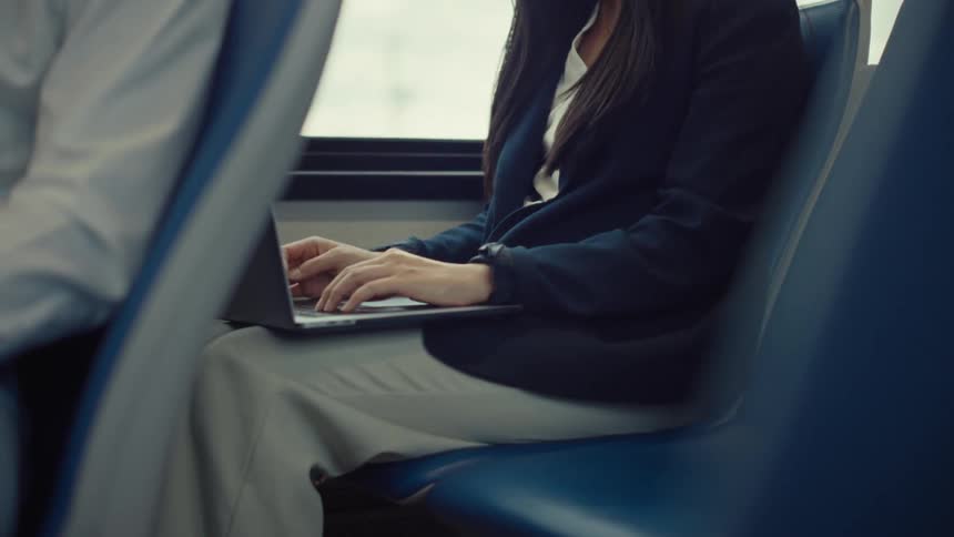 A person is sitting on a blue seat in a vehicle working on a laptop