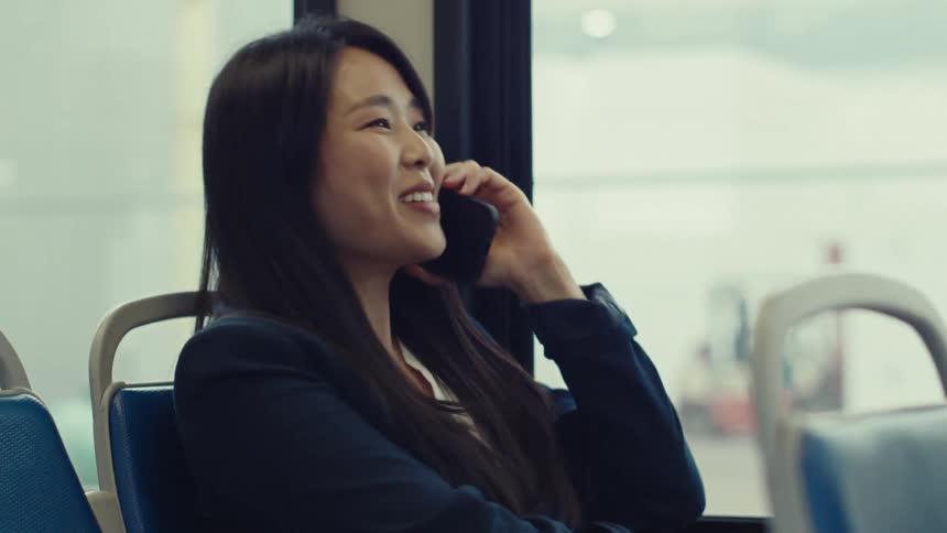 Woman riding public transportation smiles while talking on her smartphone