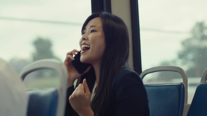A woman sitting on a train laughs as she talks on her cellphone
