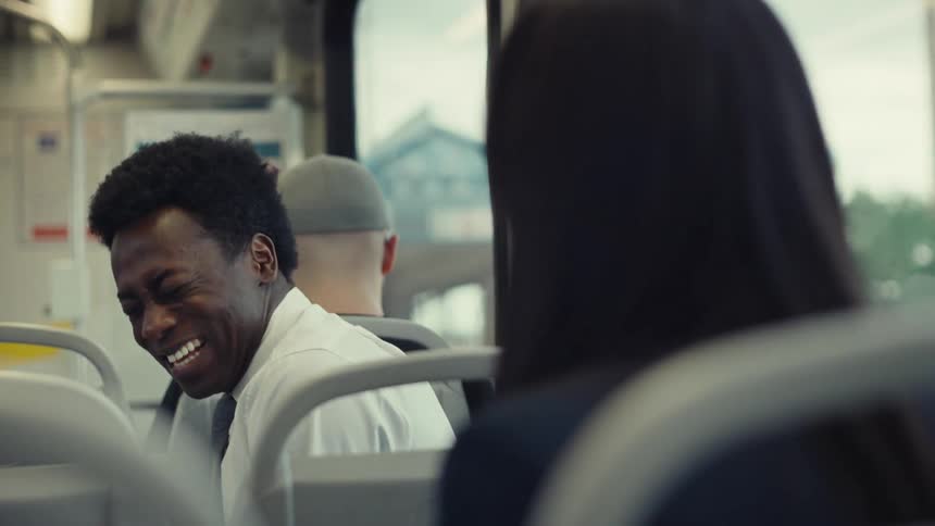 A man and woman laugh as they talk on a train
