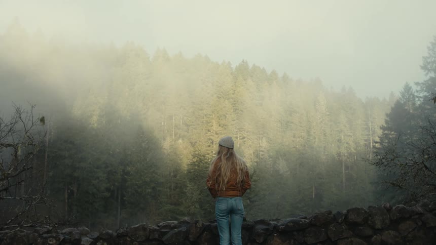A woman looks over at the forest covered in heavy fog