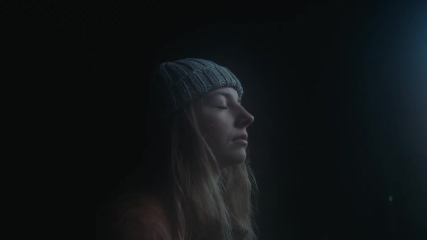 A woman with long hair wearing a hat closes her eyes as she sits quietly