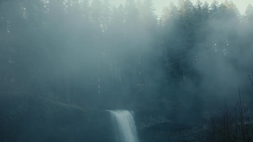Water pours over a cliff in a waterfall in a hazy forest