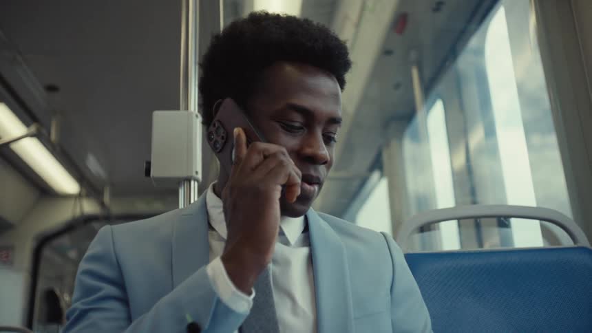 A man in a blue suit talks on his smartphone while traveling on the train