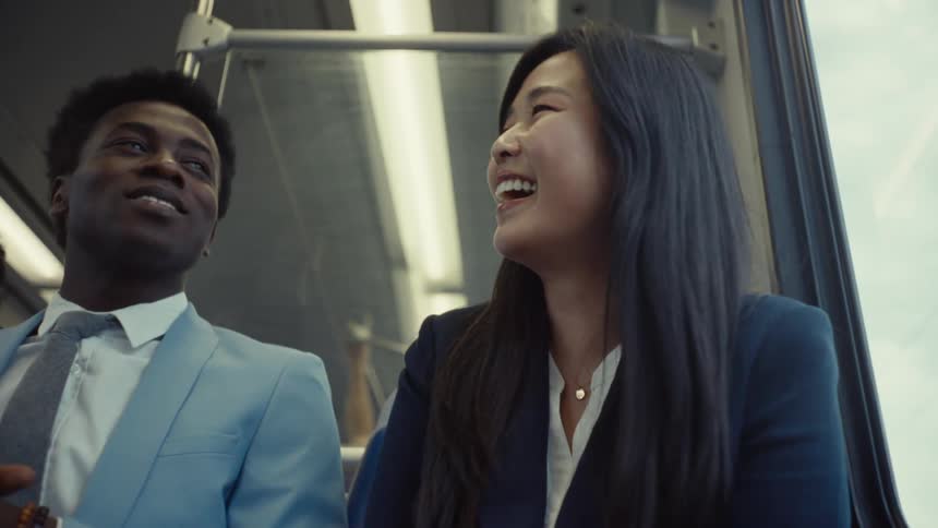 A man and woman sit together on a train while they laugh and talk