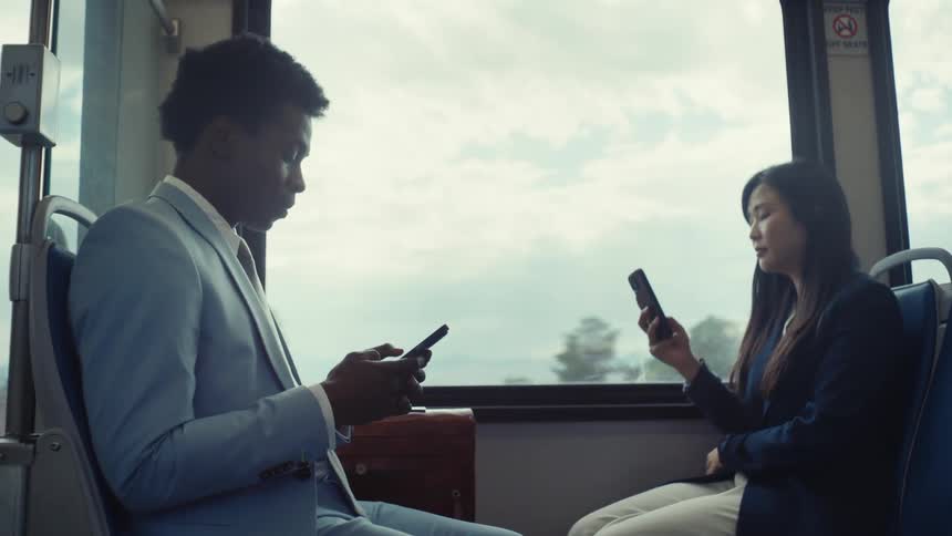 A man and woman use their cell phones while riding a train