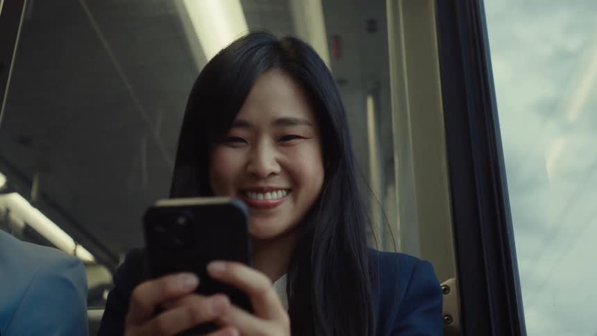 A woman with long dark hair is enjoying herself while using her smartphone during a train ride