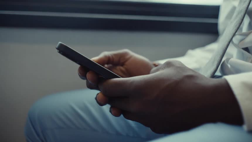 A person is sitting on a train holding a smartphone with both hands