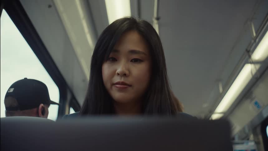 A woman with straight hair and a navy blue blazer opens her laptop while journeying on a train