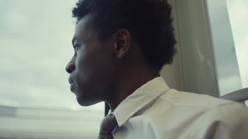A man in a white shirt and tie is sitting and looking out of a train window