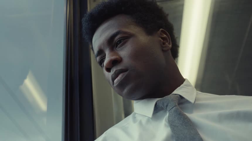 A man dressed nicely with a tie stares out a window on a train