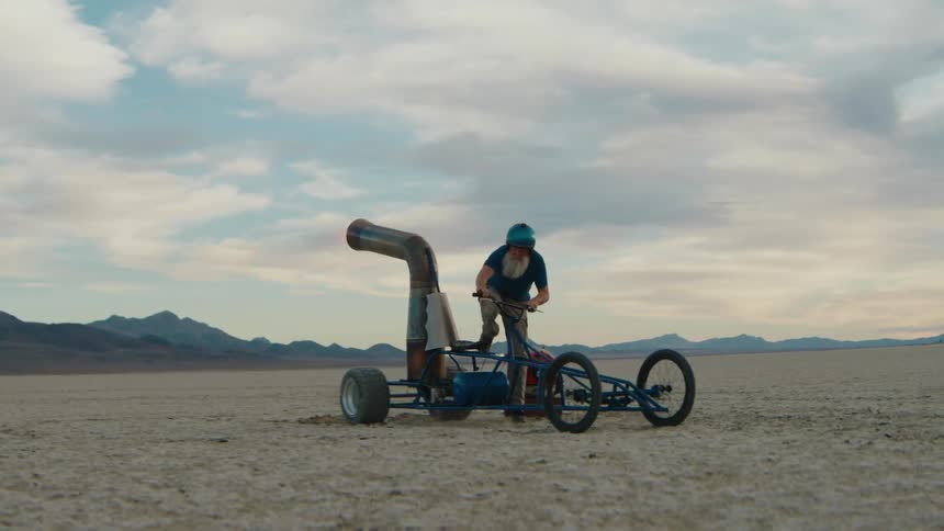 Older man drives a combustion thrust powered cart across the desert on a cloudy day