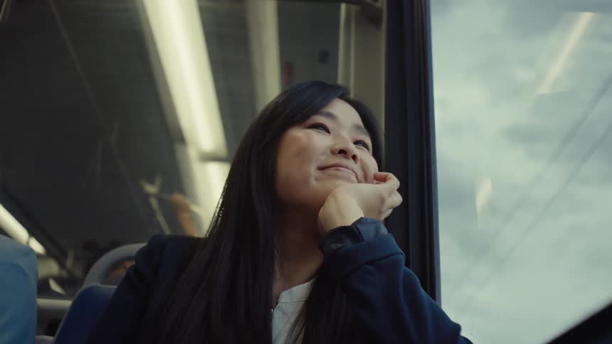 A woman with long black hair rests her head against the train window laughing softly