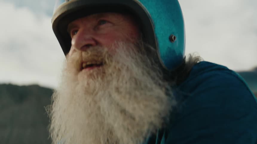 Man with long white beard wears blue helmet while walking outdoors