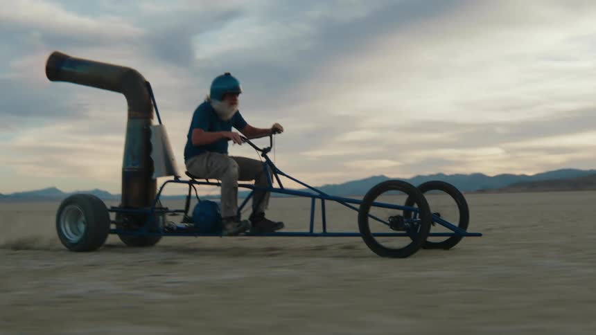 A man is riding a homemade motorized buggy vehicle in the desert