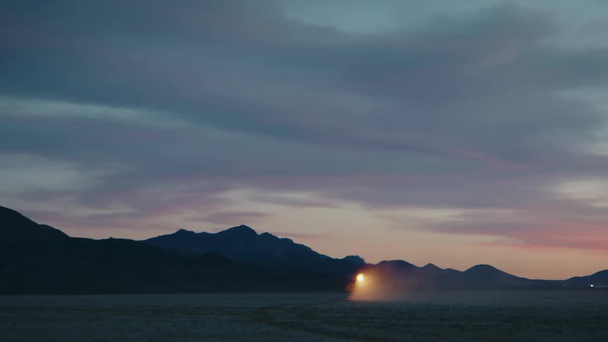 A man rides a homemade vehicle across a vast sandy landscape at sunset propelled by a fiery blast