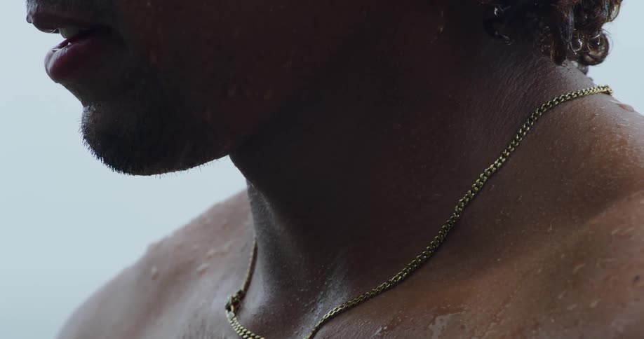 A closeup of a shirtless persons neck adorned with a gold necklace and glistening with moisture