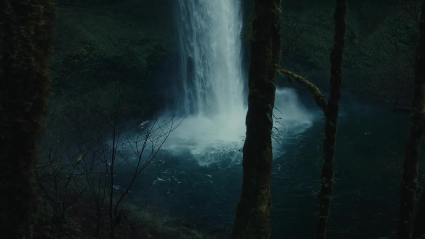 A tall waterfall pours over a cliff face in an evergreen forest
