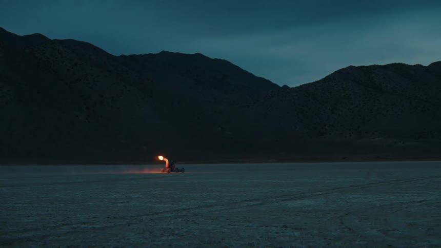A recreational vehicle drives in the desert with flames coming from the muffler