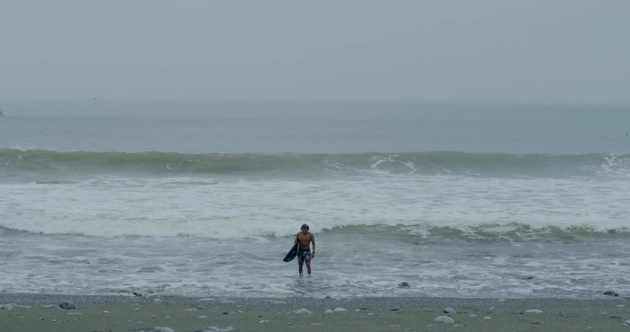 A man walks out of the ocean carrying a surfboard