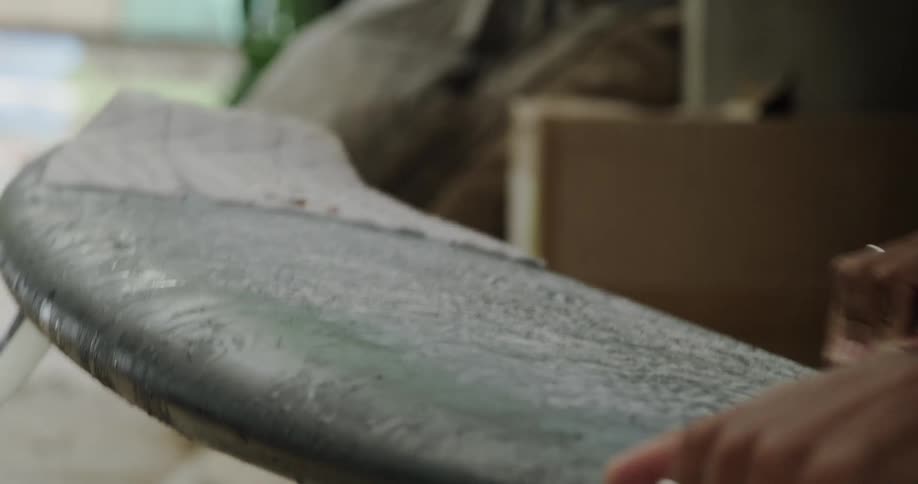 A person waxing the surface of a surfboard creating a smooth even finish