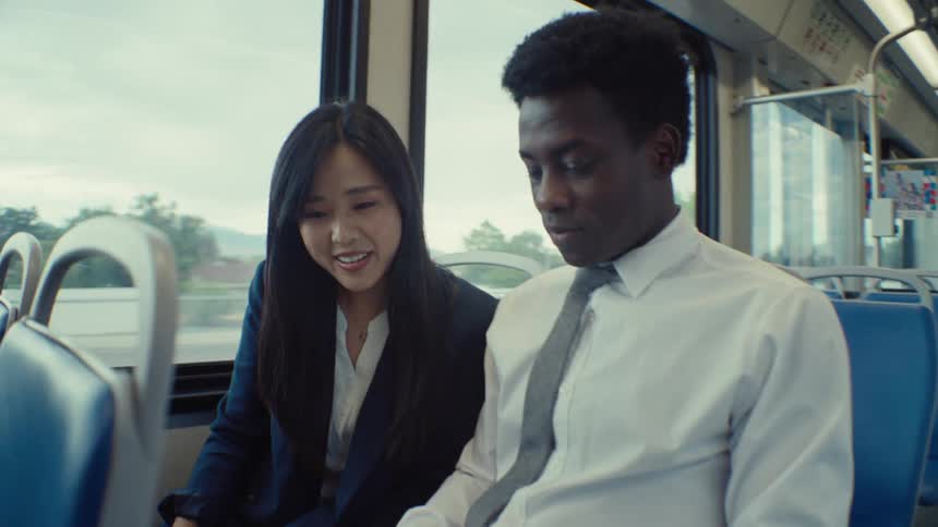 A man and woman talk and look at a laptop as they ride the train