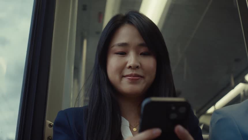 Woman sitting on a bus smiles while scrolling on her smartphone