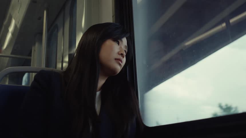 A young asian woman rides on a commuter train on a cloudy day