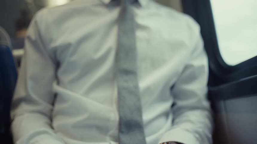 A person wearing a dress shirt and tie is using a smartphone on a train eventually setting it down