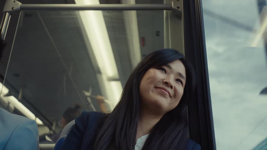 Woman riding on the bus looks out the window with a smile after looking at her smartphone screen