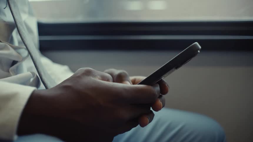 A man in a light blue suit types on his smartphone while riding the bus