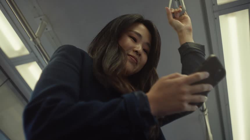 Woman holds a handle and scrolls on her smartphone while standing on public transit