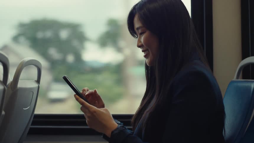 A woman smiles as she uses her cell phone on the train