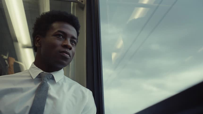A man gives a small smile as he looks out the window of a train