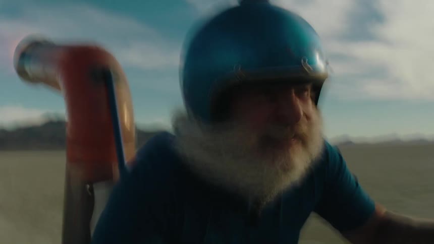 Man in blue helmet and white beard moving fast in a vehicle or equipment with an exhaust pipe spewing flames