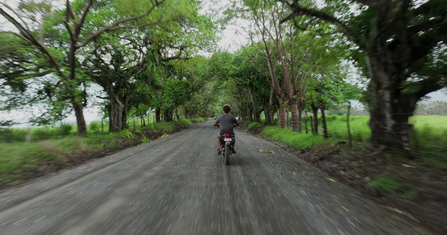An adult rides a motorcycle on a gravel road through a grassland on a summer day