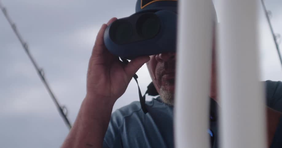 A man is looking through his binoculars on a boat
