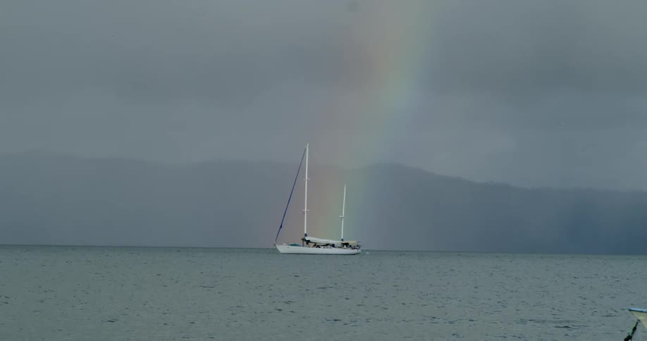 A rainbow runs behind the docked sailboat