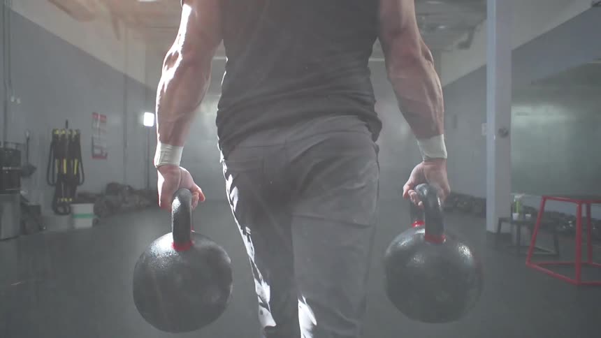 A man carries two kettlebells through a gym
