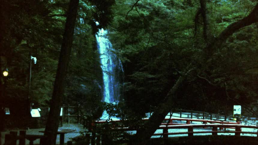 Scene of a waterfall surrounded by dense vegetation and a red bridge in the foreground