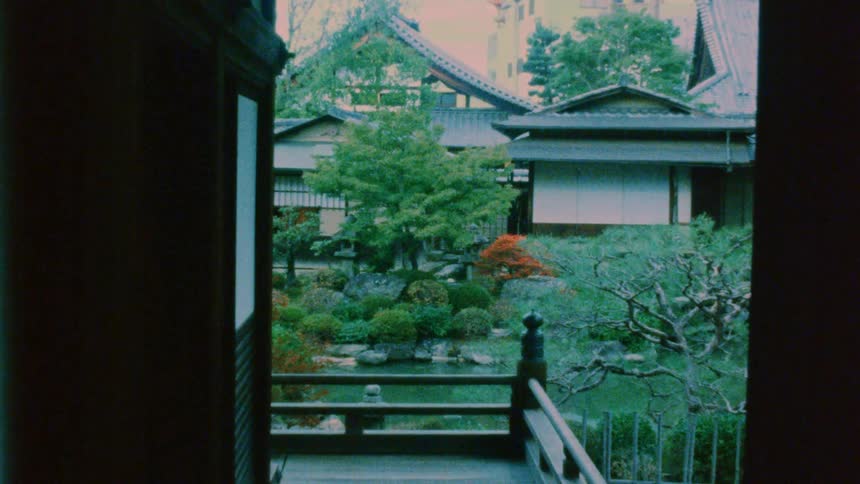 A yard is shown from the balcony of a house looking onto another house across from it