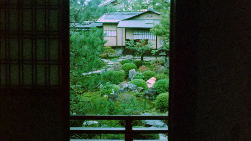 View of a traditional japanese garden through a door with carefully pruned shrubs decorative rocks and a house in the background