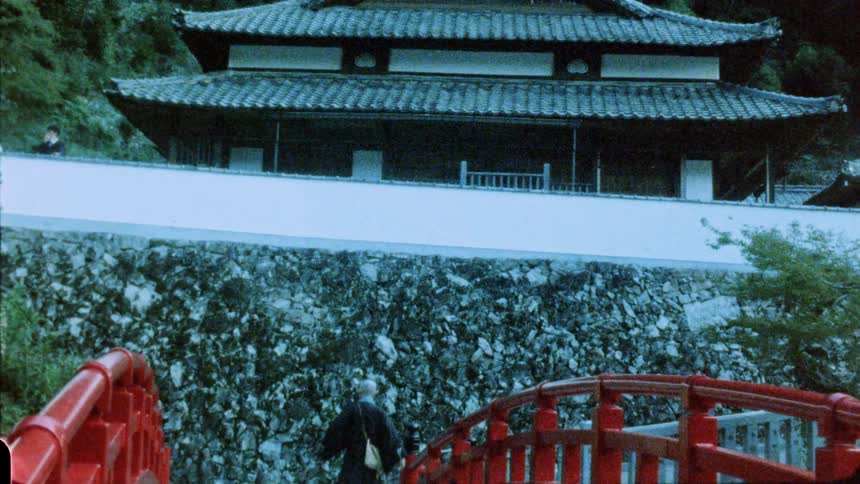 A man walks across a snowy bridge toward a building