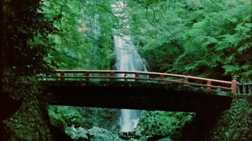 A man walks past a bridge that is near a waterfall