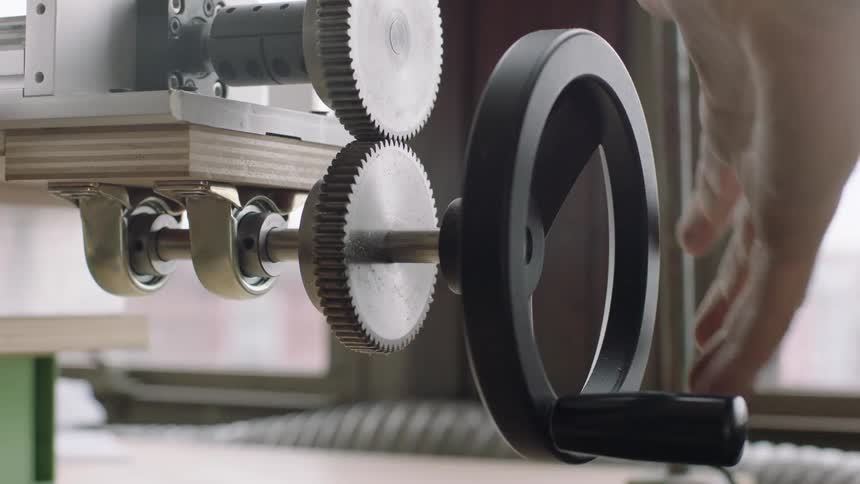 A man with white hair on his arm adjusts the gears on a machine