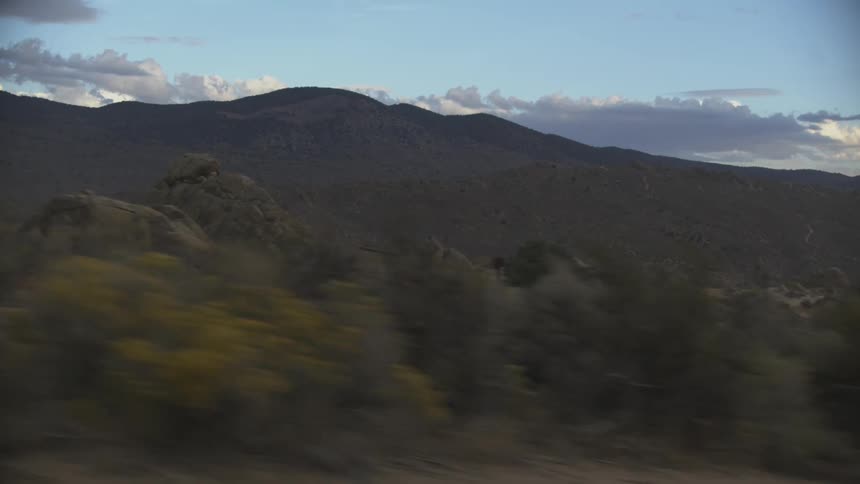 Mountainous landscape at dusk with dark hills in the background partly cloudy sky and blurred vegetation