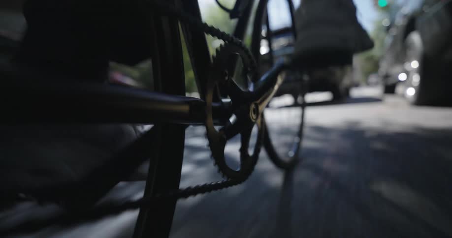 A person gets on a bike and rides down the street lined with cars