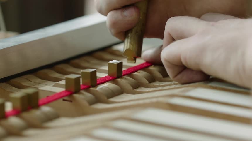 A piano technician carefully adjusts the hammers and strings of a grand piano