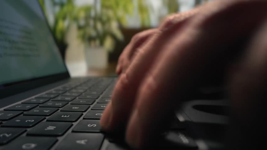 A man is typing fast on a laptop keyboard